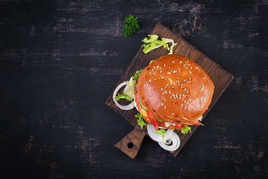 Hamburger with chicken burger meat, cheese, tomato, cucumber and lettuce on wooden background. Tasty burger. Close up. Top view
