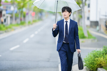 雨で傘をさすスーツの男性