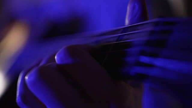 Hand of woman touching strings of guitar performing on stage illuminated by dark purple light. Musician enjoys playing musical instrument extreme closeup