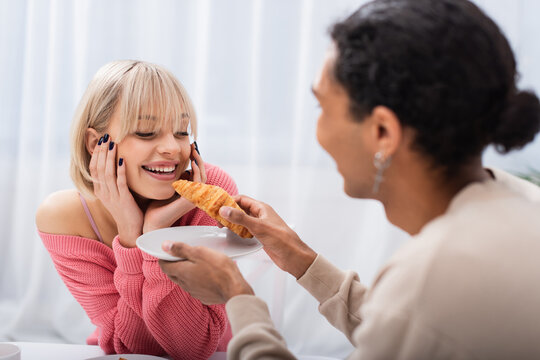 blurred african american man feeding blonde girlfriend with croissant.