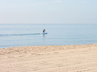 Fototapeta na wymiar Surfeur pagayant sur la mer en bord de plage de sable
