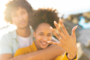 Cheerful excited woman showing off her engagement ring with african american boyfriend at beach