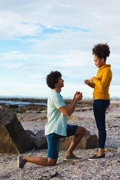 Young afro man with ring box proposing african american girlfriend while kneeling at beach