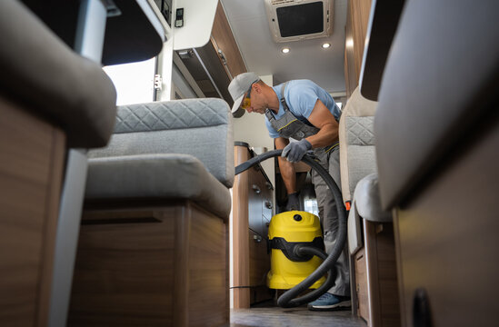Cleaning Motorhome Camper Van Interior. Caucasian Worker in His 40s with Industrial Grade Vacuum Cleaner. Recreational Vehicles Theme.