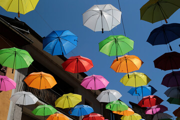 Fototapeta na wymiar Aufgehängte Regenschirme in der Fußgängerzone in Embrun in Frankreich an einem Tag mit blauen Himmel 