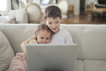 brother and sister use a computer sitting on the sofa