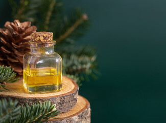 Glass bottle with conifer essential oil near fir branches and pine cones on green close up