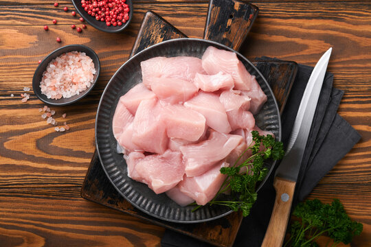 Raw chicken breast sliced or cut pieces on wooden cutting board with herbs and spices on old wooden table background. Raw chicken meat. Top view with copy space. Mock up.