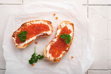 Red caviar sandwiches. Salmon red caviar in bowl and sandwiches on marble plate on old gray cracked tile table background. Top view. Copy space.