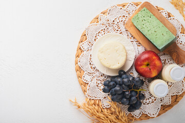 Shavuot jewish holiday celebration. Milk and cheese, ripe wheat and fruits, blue wooden background. Dairy products over white concrete background. Shavuot concept. Top view. Mock up.