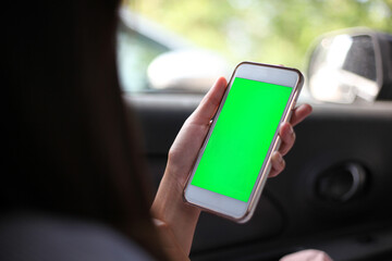 Woman's hand holding a smartphone while sitting in a car against a green screen area.