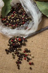 A mixture of peppers on a background of burlap. A spoonful of allspice peas. Dry fresh spices