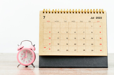 Naklejka premium July 2022 Desk calendar with pink alarm clock on wooden table.