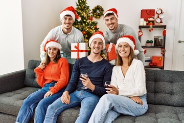 Group of young people celebrating christmas holding gift drinking wine at home.
