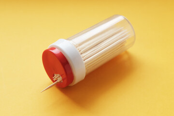 Plastic jar with a red lid with wooden toothpicks lies on a yellow background