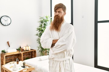 Redhead man with long beard wearing bathrobe at wellness spa skeptic and nervous, disapproving expression on face with crossed arms. negative person.
