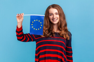 Optimistic woman wearing striped casual style sweater, showing flag of European union, looking at...
