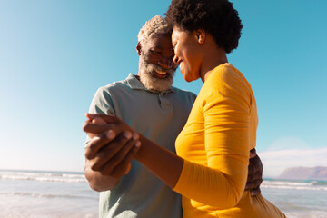 Happy romantic african american couple dancing at beach against clear blue sky on sunny day
