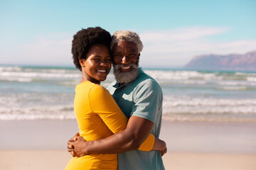 Portrait of happy african american couple embracing while standing against sea and sky in summer