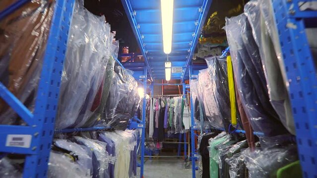 Warehouse with clothes. The clothes are hung in rows in the warehouse. Clothes in the warehouse of the factory. industrial interior