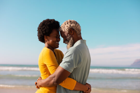 Side view of happy romantic african american couple embracing and dancing against sea and blue sky