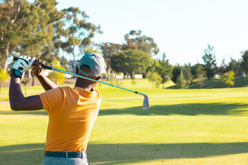 Rear view of african american young man wearing cap playing golf against clear sky at golf course