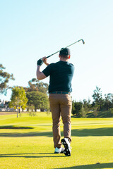 Obraz premium Rear view of caucasian young man hitting with golf club against clear sky at golf course in summer