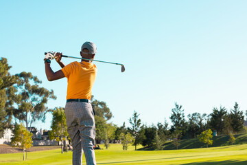 Rear view of african american young man playing golf against clear sky at golf course during summer