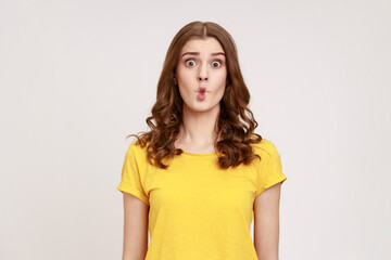 Portrait of charming funny teen girl with wavy hair in yellow T-shirt shows fish face grimace with...