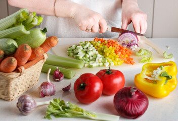 Women's hands chop fresh vegetables for cooking. Carrots, zucchini, celery, bell pepper, tomatoes,...