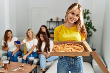 Group of young friends woman having party sitting on the sofa. Girl smiling and holding pizza at...