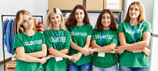 Group of young volunteers woman smiling happy standing holding hands at charity center.