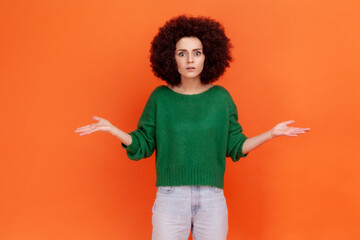 Angry woman with Afro hairstyle wearing green casual style sweater standing with raised hands and...