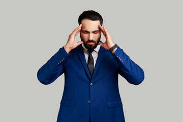 Bearded man frowning and clasping sore head, suffering intense headache, having unbearable...