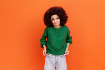 I'm bankrupt! Unhappy poor woman with Afro hairstyle in green sweater showing empty pockets and...