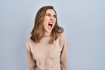 Young woman standing over isolated background angry and mad screaming frustrated and furious, shouting with anger. rage and aggressive concept. - obrazy, fototapety, plakaty