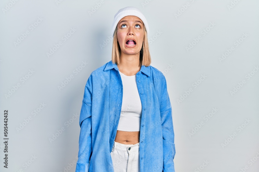 Sticker Beautiful blonde woman wearing wool hat angry and mad screaming frustrated and furious, shouting with anger. rage and aggressive concept.