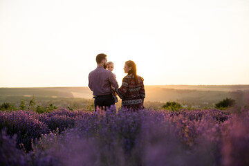 Happy family mother father and baby daughter standing on a lavender field. Mom dad and a little child hugging on a field in the morning