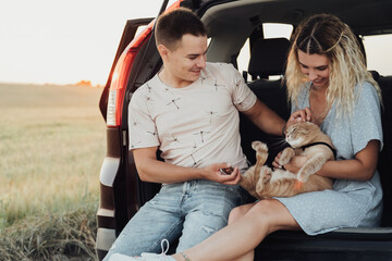 Young Woman and Man Sitting in Trunk of the Car with Pet, Happy Couple with Their Red Cat Enjoying Road Trip