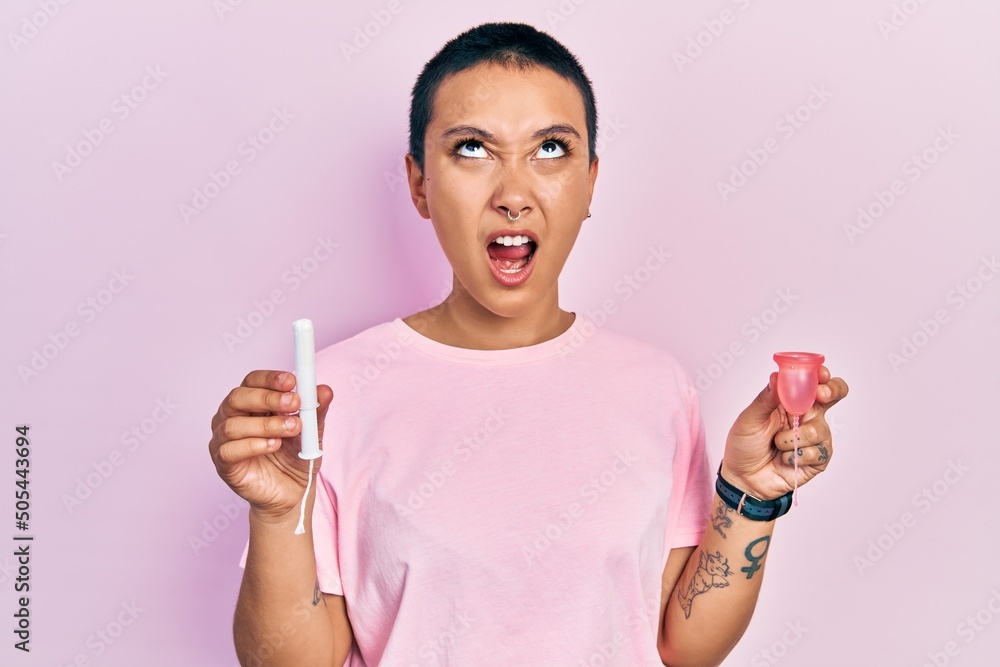 Sticker beautiful hispanic woman with short hair holding menstrual cup and tampon angry and mad screaming fr