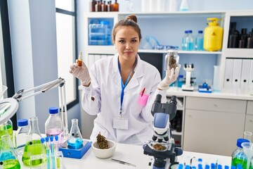 Young hispanic woman doing weed oil extraction at laboratory relaxed with serious expression on face. simple and natural looking at the camera.