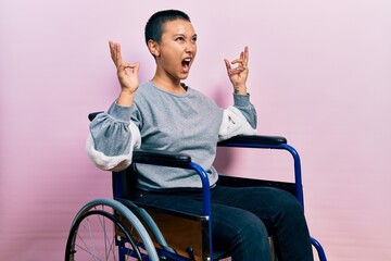 Beautiful hispanic woman with short hair sitting on wheelchair crazy and mad shouting and yelling with aggressive expression and arms raised. frustration concept.