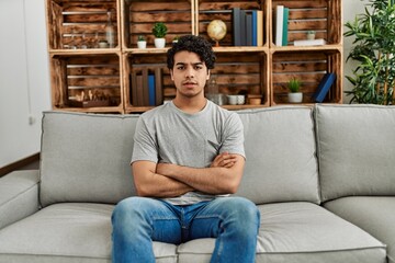 Young hispanic man wearing casual clothes sitting on the sofa at home skeptic and nervous,...