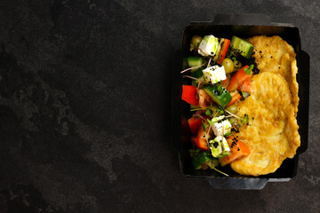 Healthy food delivery concept. Chicken schnitzel with Greek salad in an eco paper container on a...