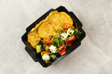 Healthy food delivery concept. Chicken schnitzel with Greek salad in an eco paper container on a...