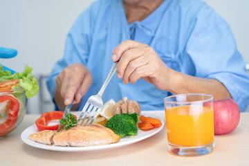 Fototapeta na wymiar Asian senior or elderly old lady woman patient eating Salmon steak breakfast with vegetable healthy food while sitting and hungry on bed in hospital.