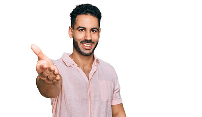 Hispanic man with beard wearing casual shirt smiling friendly offering handshake as greeting and welcoming. successful business.