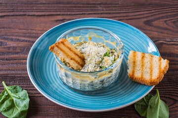 Hot appetizer, spinach and cream cheese dip in a transparent form on a blue plate on a brown wooden background. Served with toasted wheat bread.