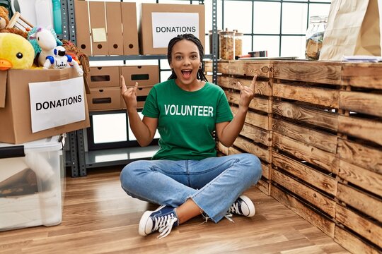 Young african american woman wearing volunteer t shirt at donations stand shouting with crazy expression doing rock symbol with hands up. music star. heavy concept.
