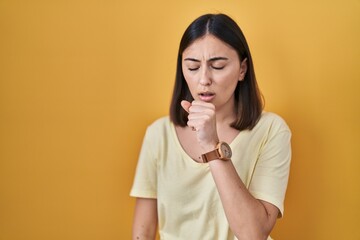 Hispanic girl wearing casual t shirt over yellow background feeling unwell and coughing as symptom...